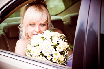 Young blonde with flowers in the car. The bride looks out of the car window
