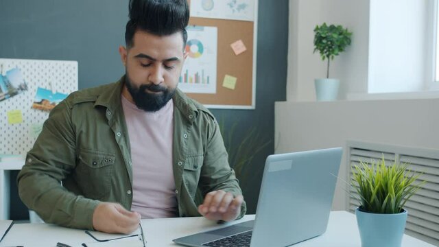 Middle Eastern guy is using laptop then hitting table and leaving feeling unhappy and disappointed working in office alone. Negative emotions and technology concept.