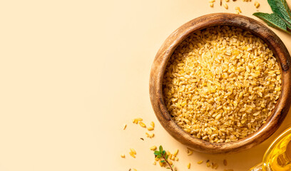 Dry uncooked bulgur in a wooden bowl on a beige background top view. Healthy food, Middle Eastern food. Free space for text