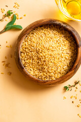 Dry uncooked bulgur in a wooden bowl on a beige background top view. Healthy food, Middle Eastern food. Free space for text