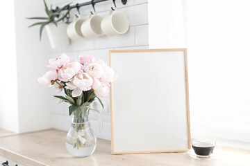 Vertical frame mockup on a wooden table in the kitchen. Glass vase with a bouquet of pink peonies...