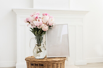 Vertical frame mockup on a wooden table in the kitchen. Glass vase with a bouquet of pink peonies. Scandinavian style interior.