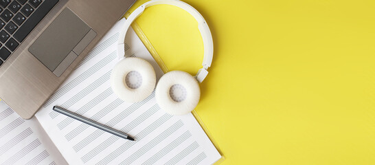 Top view open music book, headphones pen and laptop on yellow background. workplace. banner