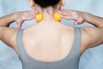 Young woman massages her neck with trigger point tennis ball used for muscle pain relieve and...