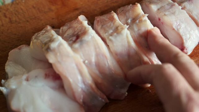 Close up shot of slices of monkfish arranged on a cutting board. One hand touches and checks the slices. Mediterranean diet, food and health concept.