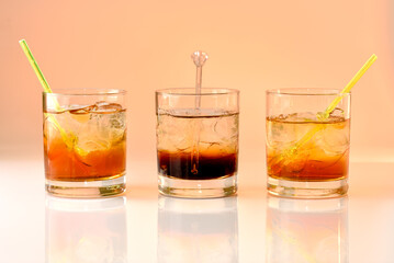 three cocktails on orange background, god mother, Black Russian and god father in glass with ice