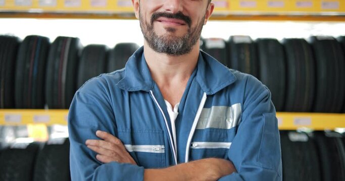 Portrait of Mechanic in work uniform looking camera at car tires shop service, Specialist tire fitting in the car service, checks the tire and rubber tread for safety.