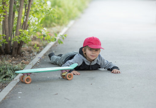 A Child Has Fallen Off A Skateboard And Is Lying On The Road. Spring Concept