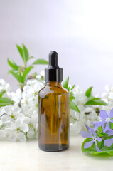 A brown glass bottle with a dropper containing essential oils or serum with fresh flowers. Natural products for skin care.
