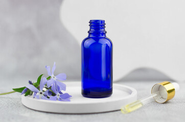 A bottle of essential oils stands on a podium with flowers. Natural skin care concept. Natural herbal products. Cosmetic pipette on gray background
