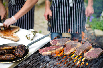 Steaks grilling on open flame and chef hands slicing steak in background