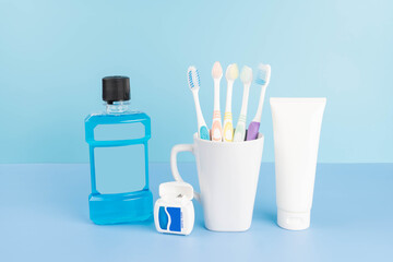 Oral care products set for healthy teeth and gums. Toothbrushes in glass with toothpaste, mouthwash and dental floss on blue background.
