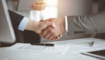 Business people shaking hands finishing contract signing in sunny office, close-up. Handshake and marketing
