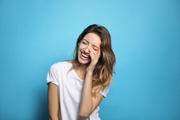 Fototapeta na wymiar Cheerful young woman laughing on light blue background
