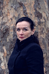 eautiful woman in her 50s with black coat standing in front of tree