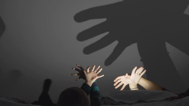 Detail of child and parent hands making shadows on wall, night tale