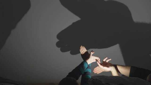 Parent and child hands play with hands making shadows on wall
