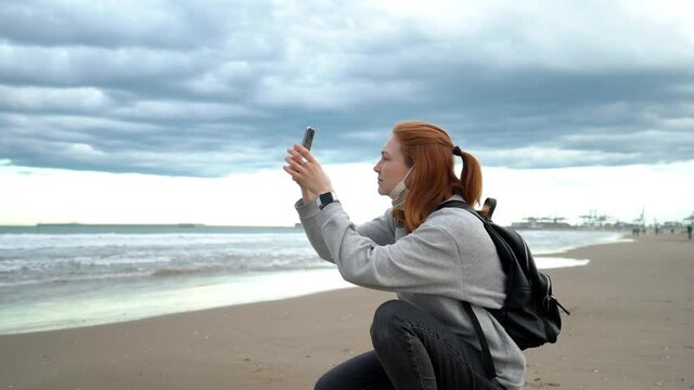 A red-haired girl takes pictures of beautiful clouds the sea on her phone.