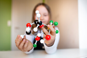pretty young schoolgirl with black dungarees sits in her room and learns on a model for molecules