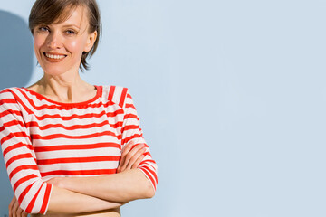 Happy cheerful young woman with short hair, natural makeup over light blue background. Indoor portrait of beautiful brunette young woman wearing bright clothing	