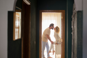 Romantic couple kissing at home - happy relationship man and woman indoor - husband and wife kiss with love and passion with window light in background - concept of happiness and togetherness