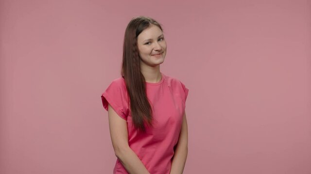Portrait of fashion model coquettishly looking at camera and smiling. Young brown haired woman with long hair in pink t-shirt poses on pink studio background. Close up. Slow motion ready 59.94fps.