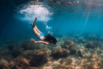 Woman with diving mask posing underwater in transparent sea with sun rays