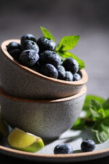 Fresh berries with drops, blueberries with lime, mint in a bowl on a gray background. Summer, freshness, sunshine. Background image, copy space