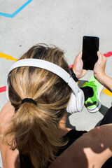 Fototapeta premium Sportsman With His Smartphone. Portrait Of A Sportswoman Sitting On An Urban Court And Using Her Smartphone. She Wears Headphones