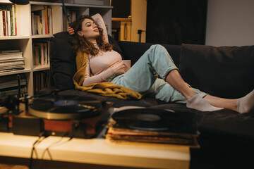 woman relaxing on sofa at home while listening records on gramophone
