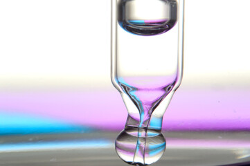 Cosmetic pipette with drops of transparent liquid and a jar, close-up on a colored background.