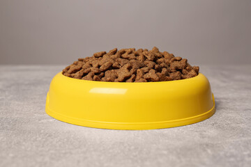 Dry food in yellow pet bowl on grey surface