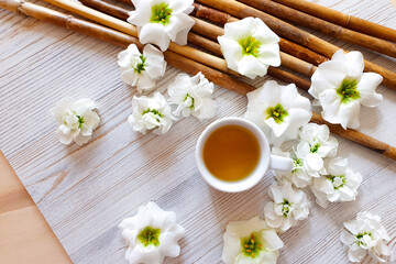 Chinese herbal tea in white cup, brown bamboo and white flowers on wooden table with copy space. Top view.