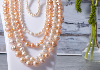 Iridescent natural white and beige pearl necklaces hang close up on a gray background. Pearl texture, luxurious jewelry. 