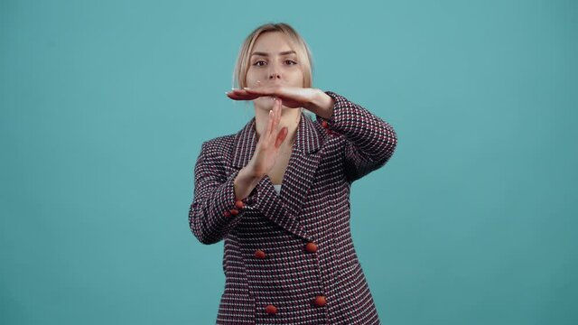 The portrait of a blonde-haired girl who seriously shows her stop sign with her hands.Isolated on a turquoise background. The concept of life. People's emotions. Portrait 4k