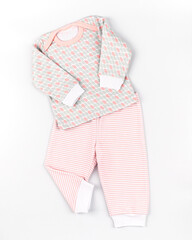 Pajamas for the baby. Laid out clothes on a white background, top photo, top view, dynamic photo. Home suit of blouse and trousers for girls in pink color made of natural knitted cotton.