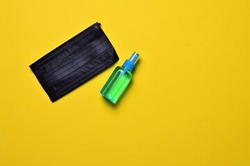 Hygienic and sanitary measures. Hand sanitizer gel and surgical mask on yellow background.