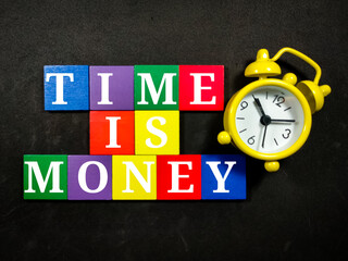 Text TIME IS MONEY with colorful wooden jigsaw and alarm clock on black background.
