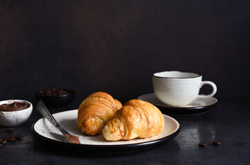 Croissant with chocolate paste and a cup of coffee, strawberries on the kitchen table. ​Traditional snack or breakfast.