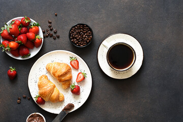 Croissant with chocolate paste and a cup of coffee, strawberries on the kitchen table. ​Traditional snack or breakfast.