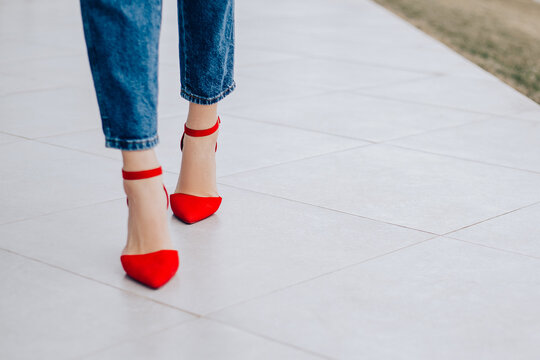 Small business owner office worker woman standing outside building legs red shoes high heels. Female successful executive girl walking on the street. Copy space. Fashion concept, blue jeans 
