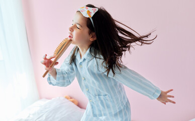 Portrait of a playful little girl in pajama holding a hair brush like microphone singing imitates herself a real singer in the morning.