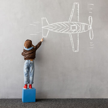 Happy kid draws a chalk airplane on the wall