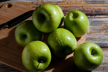 Wet green apples on a cutting board and on a wooden vintage table with a knife on the side.