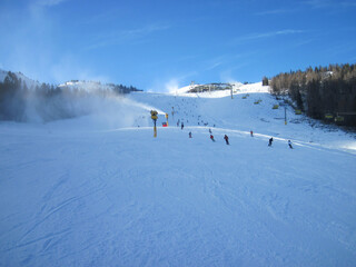 Ski slope in sunny weather, skiers and snow fog