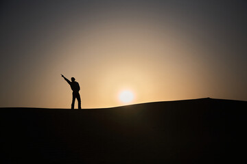 A man stands on a desert dune and makes a movement like Michael Jackson. Do you know the feeling when everything is possible? It's a great feeling. Off to the desert ;-) Sunset. Normal perspective. 