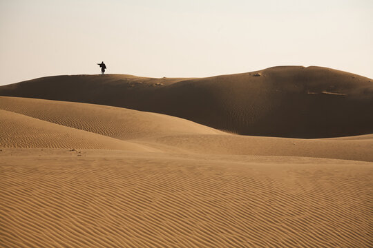 Desert dweller stands on a dune and stretches his arm to the left. In which direction is it going? Day. Normal perspective. 
