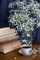 Still life with cup of tea. Simple composition photo with small white flowers and cup of black tea on a table. Beautiful morning picture. 