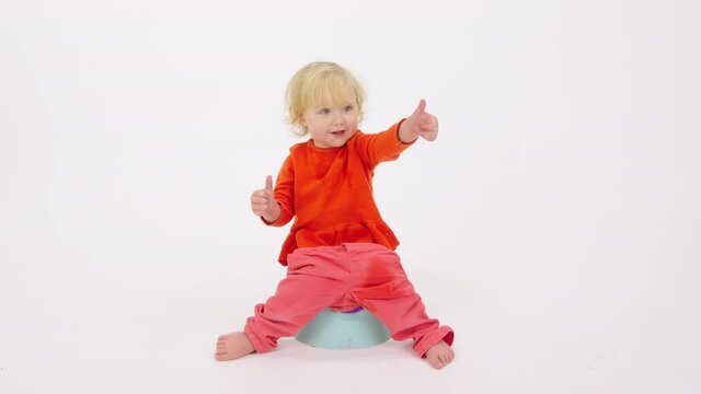 Adorable happy cheerful toddler girl sitting on potty showing thumbs up gesture isolated on white studio background. Getting baby accustomed to potty. Success, good achievement, new skill concept