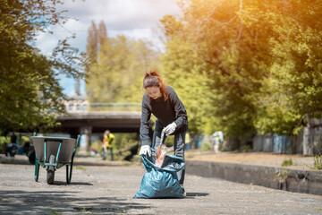 volunteer female cleaning up park and tree from plastic litter with garbage bag